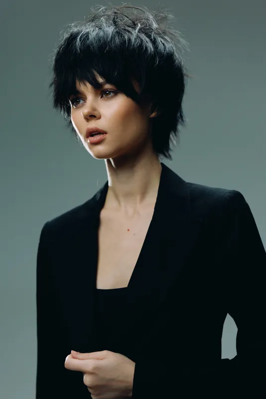Portrait of a stylish woman with short black hair in a black jacket, showing a thoughtful expression and modern fashion style.