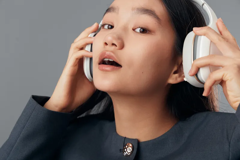 Girl, headphones, and face closeup for music listening, youth culture and lifestyle. Portrait of young female enjoying audio sound in casual outfit with grey background and modern technology device.