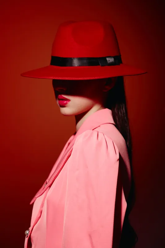 Stylish woman wearing a red hat and pink blazer poses against a red background. Bold colors and fashion-forward look emphasize creativity and beauty in style.