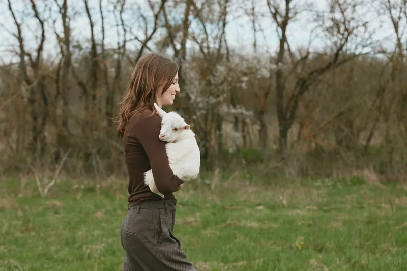 Joyful woman outdoors, holding a small dog in a sunlit field, peaceful countryside setting, candid moment, relaxed posture, natural colors, gentle breeze, everyday lifestyle scene