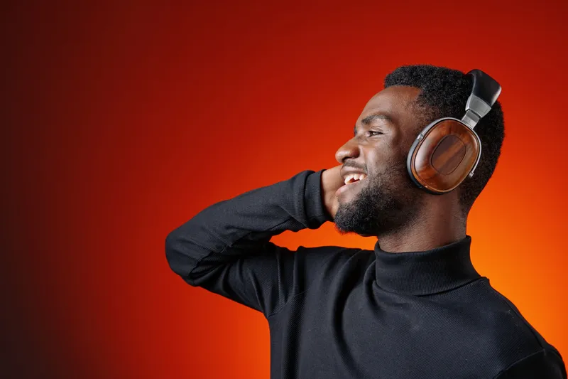 Happy young Black man enjoying music with headphones against a vibrant orange background, showcasing joy and passion for music