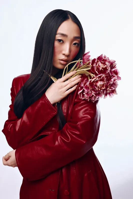Стильная азиатская женщина в красной кожаной куртке держит букет тюльпанов в солнечный день