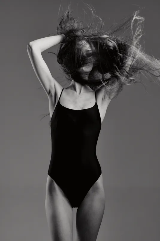 Black and white portrait of a slender woman in a black swimsuit with flowing hair and dynamic pose.