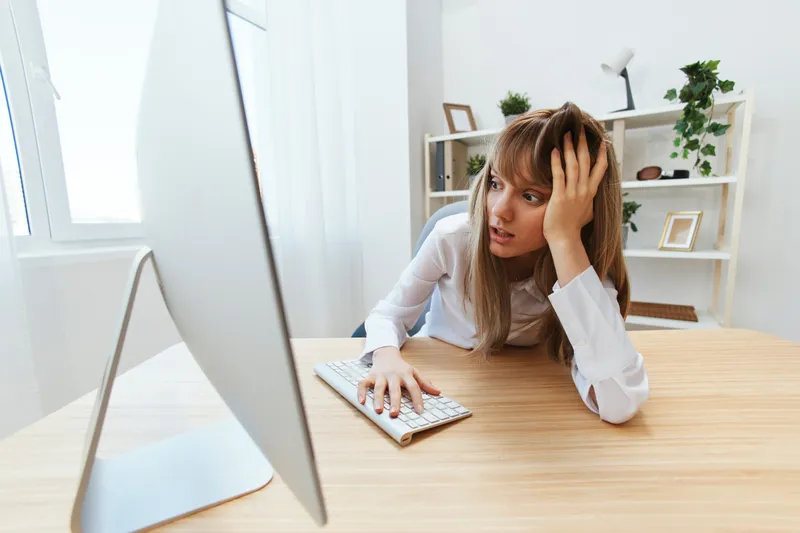 Шокированная светловолосая бизнесвумен совершила большую ошибку в отчете, смотрит на экран, опираясь на руку, сидя на рабочем месте в современном офисе