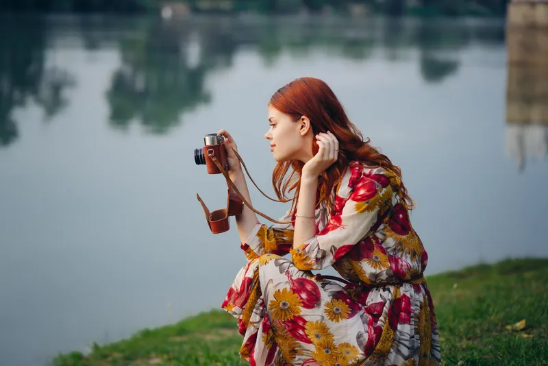 Женщина в платье с фотоаппаратом на природе, фотографирующая реку, хобби