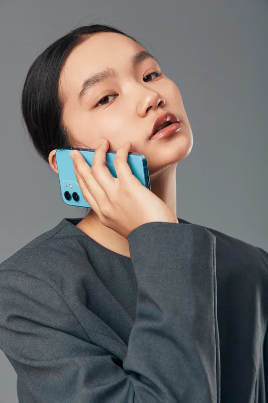 Young woman with dark hair holding blue smartphone to ear in studio. Casual clothing, neutral background, closeup portrait expressing focus and communication by phone call.