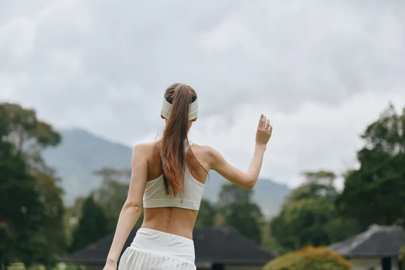 Young woman in sportswear waving outdoors, conveying a sense of fitness and freedom in a natural setting, perfect for healthy lifestyle themes