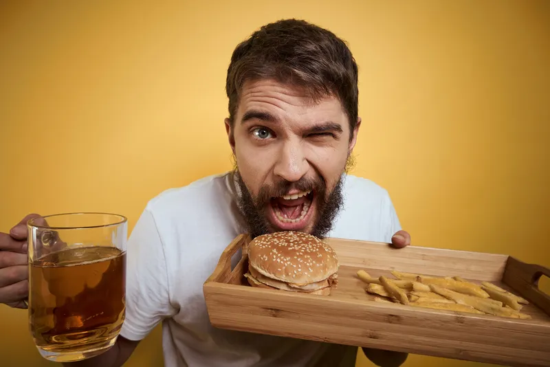 Бородатый мужчина с кружкой пива, ассоциирующийся с фастфудом, диетической едой, весельем, алкоголем и образом жизни, на жёлтом фоне