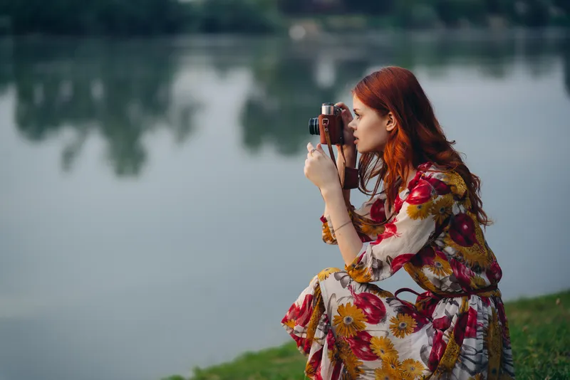 Симпатичная женщина с фотоаппаратом у озера на открытом воздухе, отдых