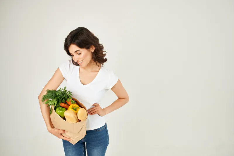 Симпатичная женщина в белой футболке с пакетом продуктов пользуется услугой доставки покупок