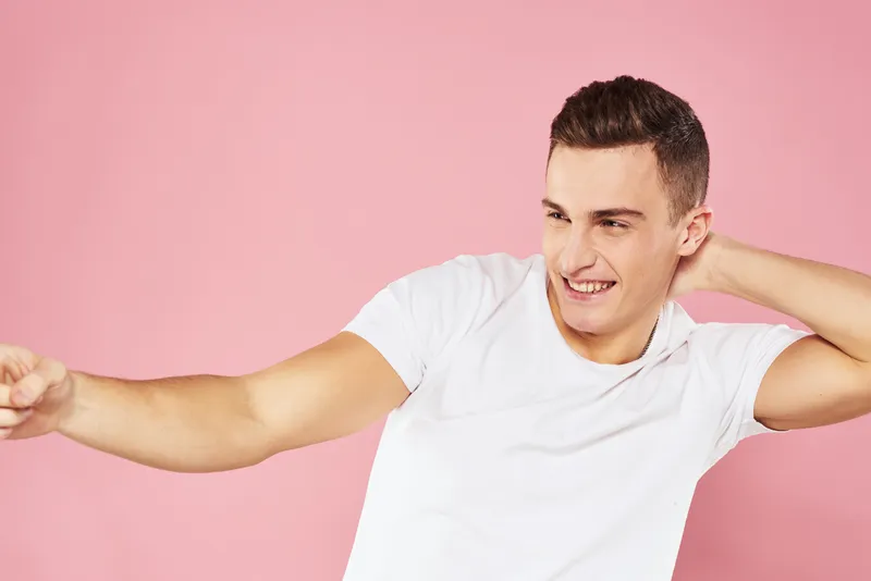 Весёлый симпатичный мужчина в белой футболке, выражающий эмоции на розовом изолированном фоне