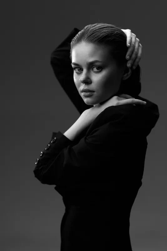 black and white portrait of a young woman with braided hair in a black outfit against a dark background