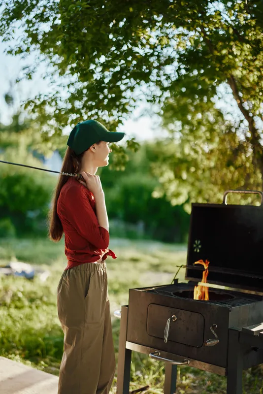 Young woman in sportswear cooking on a barbecue grill outdoors, showcasing joy and relaxation during a summer gathering