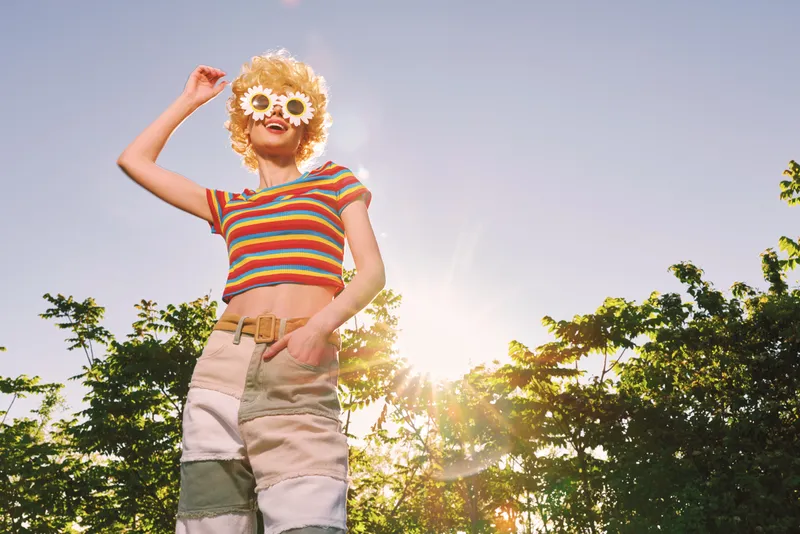 Woman lifestyle portrait with retro film color in sunny outdoors, a playful fashion scene, striped top and shorts under bright sunlight, smiling carefree in garden.