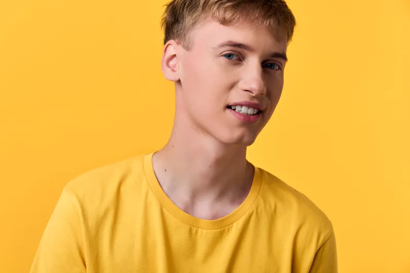 Yellow man in casual shirt with a bright background in a clean studio head shot shows a simple smile, youthful style, confidence and modern fashion for lifestyle stock photography