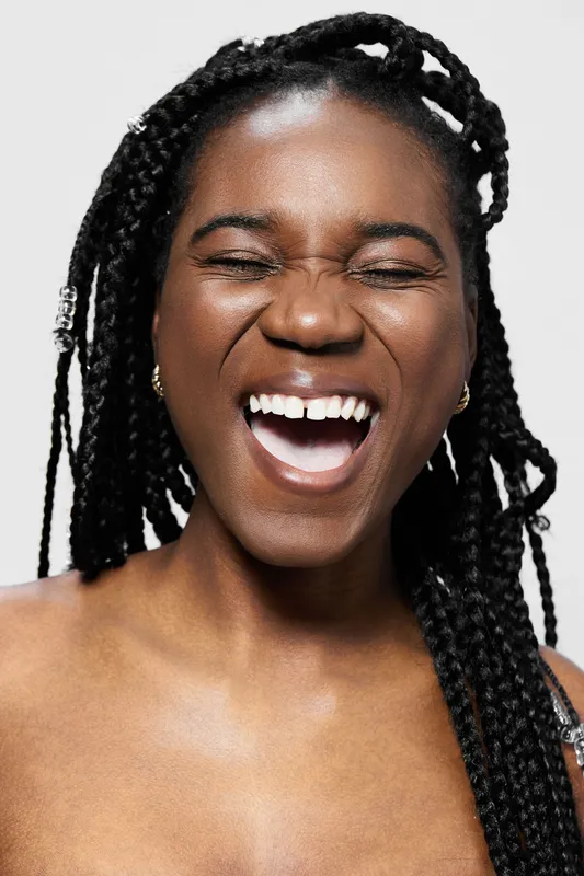 Smiling African woman with braided hair showing joy and happiness on a light background, perfect for concepts of positivity and self confidence