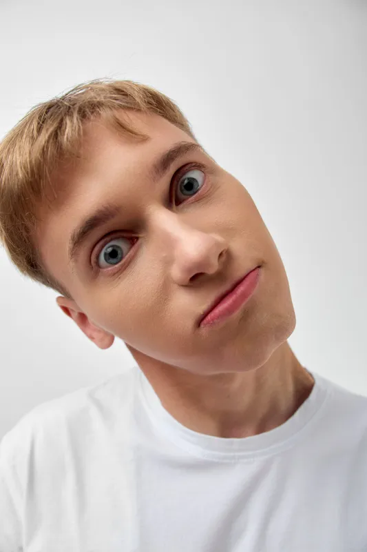 Surprised funny face tilt man expression wide-eyed closeup of a smiling adult in a white t-shirt against a plain studio background, emphasizing humor, curiosity and casual appearance