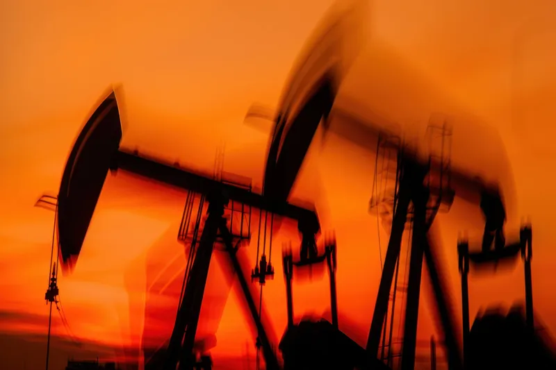 Нефтяные насосы-качалки, движущиеся на переднем плане, создающие абстрактный вид на фоне поразительного оранжевого заката