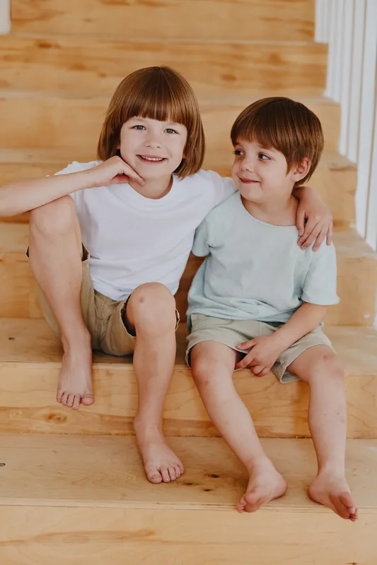 Cheerful kids sitting on wooden stairs, enjoying a moment of friendship and playfulness. Their casual outfits reflect a relaxed and warm atmosphere.