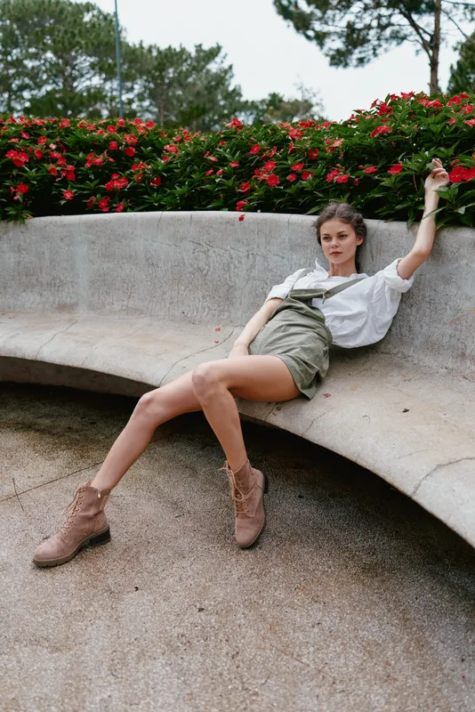 Fashionable young woman in a casual outfit sitting on a park bench surrounded by vibrant flowers, showcasing relaxed and confident emotions