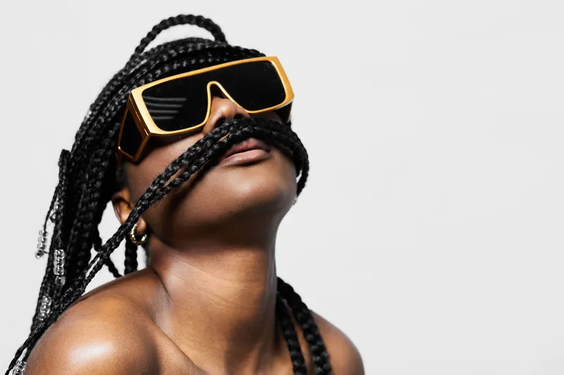 Woman with braided hair wearing oversized sunglasses, showcasing a bold fashion statement and unique style against a minimalistic background