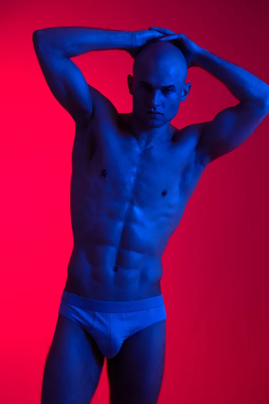 Athletic man posing under vibrant blue and red lights, embracing a striking artistic style that emphasizes body form and strength in a captivating visual presentation.