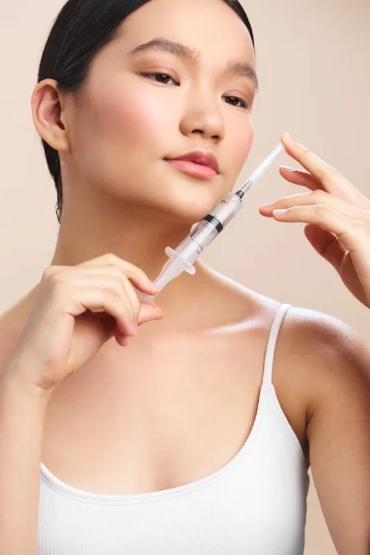 Asian woman preparing a syringe in a clinical setting, calm expression, conveying care, precision, and a professional medical atmosphere.