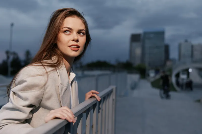 Confident businesswoman enjoying the urban atmosphere, dressed in a stylish coat, expressing positivity against a modern cityscape backdrop.