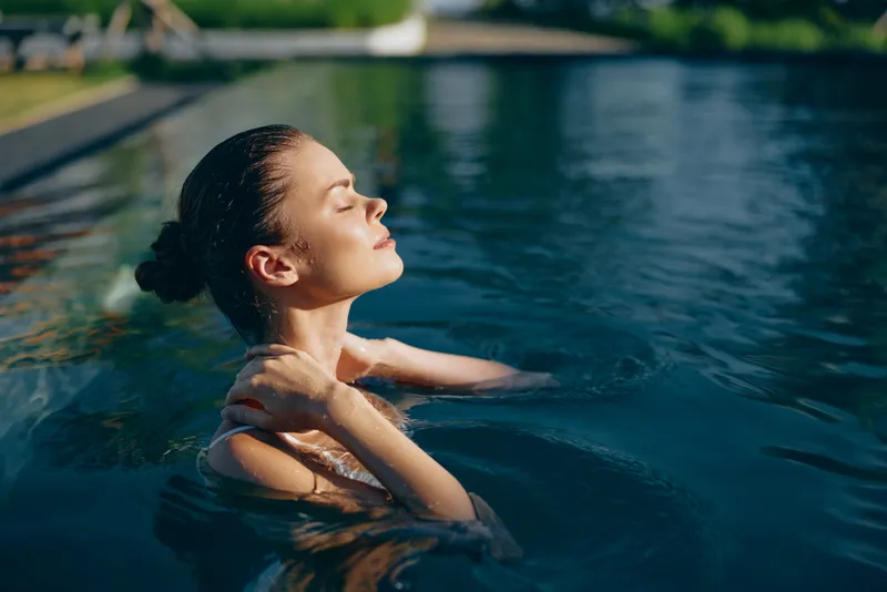 Relaxed woman floats in a sunlit pool, eyes closed, enjoying warm water, serene mood, peaceful moment, outdoor summer lifestyle, tranquil refreshment and gentle calm.
