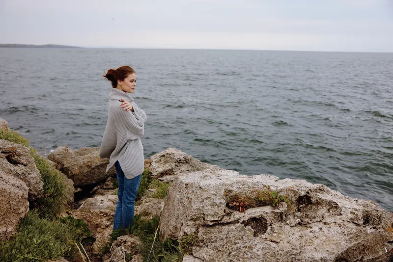 Женщина на каменистом побережье во время облачной погоды занимается пляжным туризмом