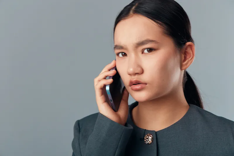 Woman, phone, serious, communication, talking, young adult, portrait, businesswoman, call, technology with focused expression on grey background for connection or conversation.