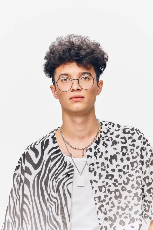 young man with glasses wearing a black and white patterned shirt, stylish haircut, modern jewelry, neutral expression, isolated background