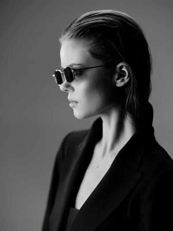 Black and white portrait of a stylish woman wearing sunglasses and a blazer, showcasing elegance and modern fashion.