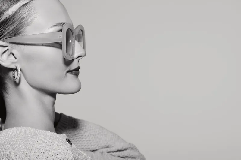Profile of a fair skinned Caucasian woman wearing large glasses and knitwear looking sideways on grey background. Concept of fashion and style.