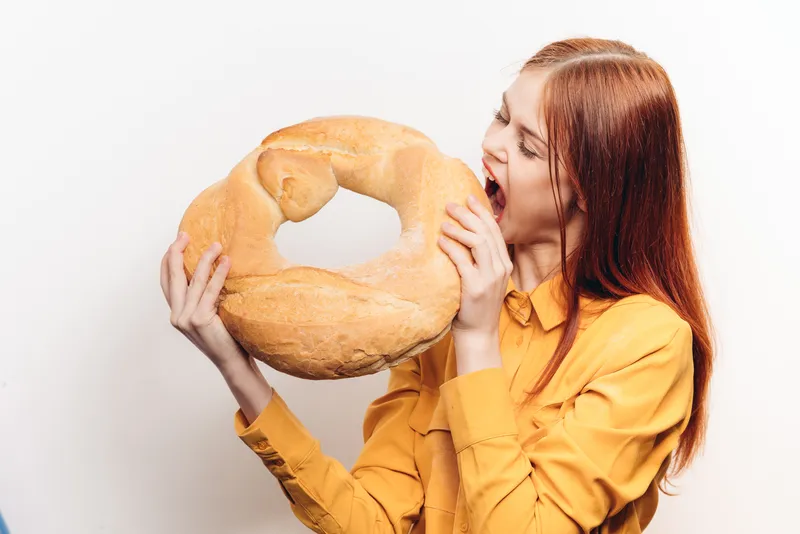 Мучное изделие, буханка хлеба и женщина в желтой рубашке на светлом фоне, кадр обрезан