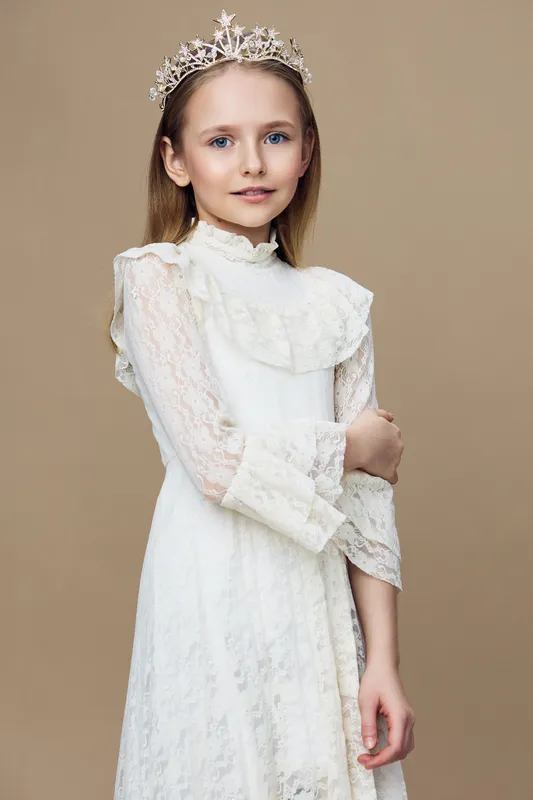 Young girl in a delicate lace dress and crown, exuding elegance and grace, posing against a neutral beige background, ideal for fashion or children s portraiture