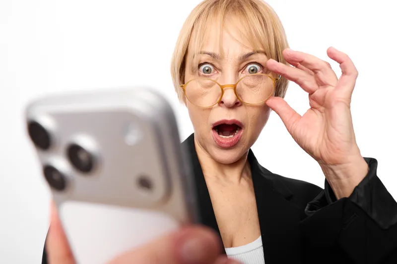 Surprised woman businesswoman on white background holding smartphone for communication, close up portrait, wearing glasses, open mouth and raised hand gesture face