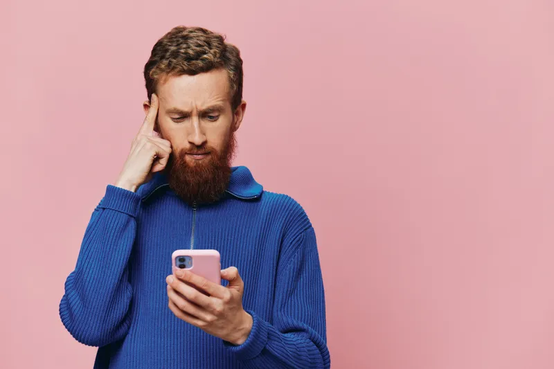 Портрет мужчины с телефоном в руках: он смотрит на него и разговаривает по телефону на розовом фоне