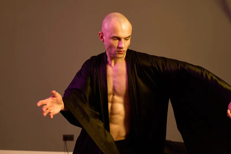 Black and white image of a man dancing gracefully in an elegant robe, showcasing strength and emotion through fluid movements and dynamic poses.