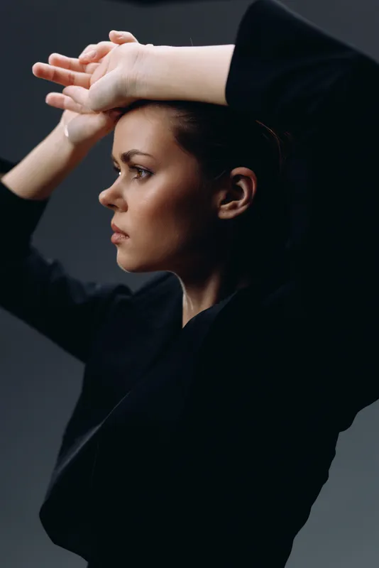 Serious woman in black clothing posing with raised arms against dark background