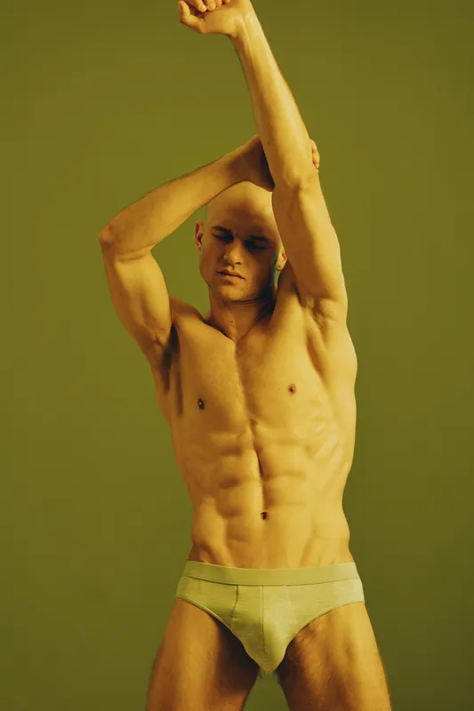 Athletic man posing gracefully against a muted green background, showcasing physical fitness and strength. This image captures an inspiring moment of passion and confidence.