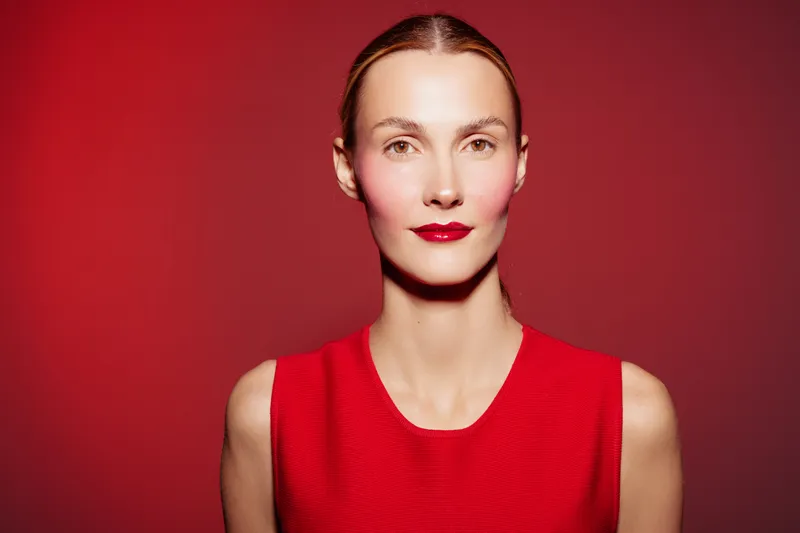 Portrait of a woman with red lipstick and red dress against a red background. Minimalist style with smooth skin and sleek hair. Concept of fashion, beauty, and elegance.