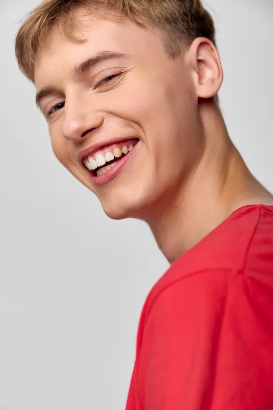 Close up of a smiling man in a red shirt, warm expression and bright eyes, casual head and shoulders shot with natural lighting, candid and friendly mood for lifestyle photography