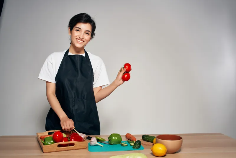 Домохозяйка в черном фартуке на кухне, свежие овощи, здоровая пища