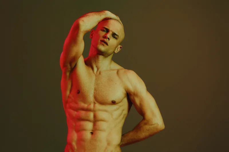 Portrait of a handsome man with an athletic build, showcasing confidence and strength against a moody, colorful background. Ideal for fitness and wellness themes.
