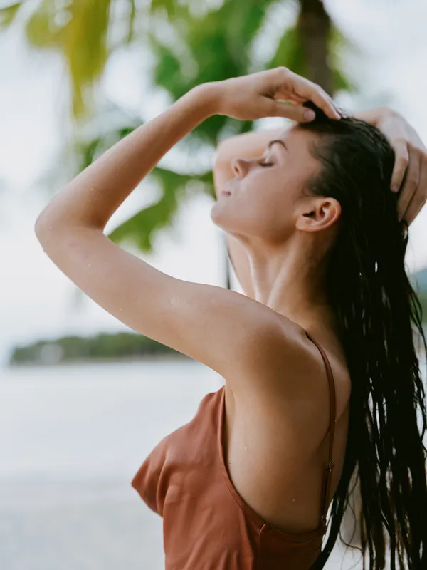 Relaxed woman with wet hair enjoying tropical beach environment, wearing a brown dress, natural light, calm and peaceful mood.