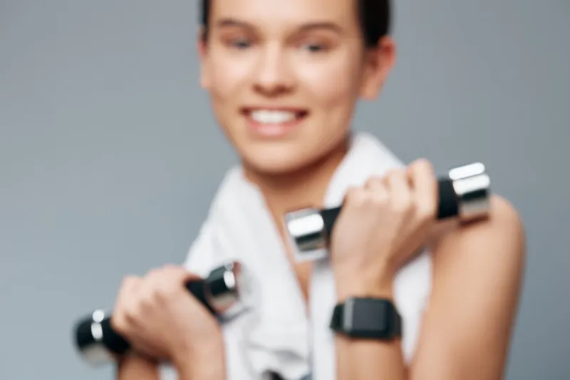 Fitness woman lifting dumbbells for workout and strength training in a gym, showcasing sport energy, focus, and healthy lifestyle through dynamic motion and confident posture in a modern studio.
