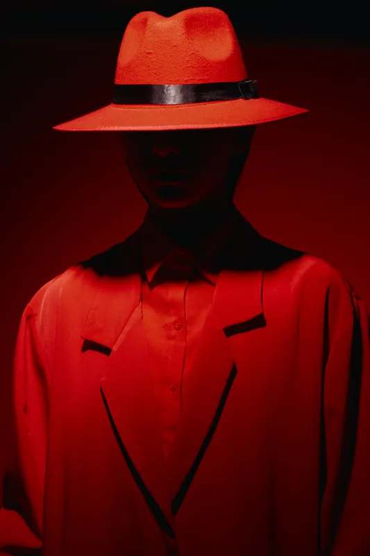 Stylish fashion portrait of a person wearing a red wide-brimmed hat and bright red coat in dramatic studio lighting. Concept of beauty, creative fashion, elegance, and mystery.