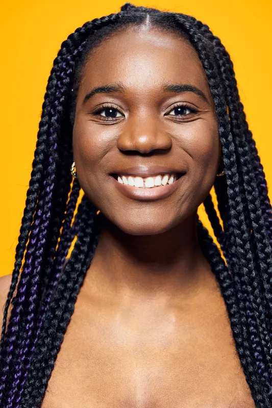 Cheerful female model with braided hair and a bright smile against a yellow background, representing joy and confidence in a vibrant and uplifting atmosphere