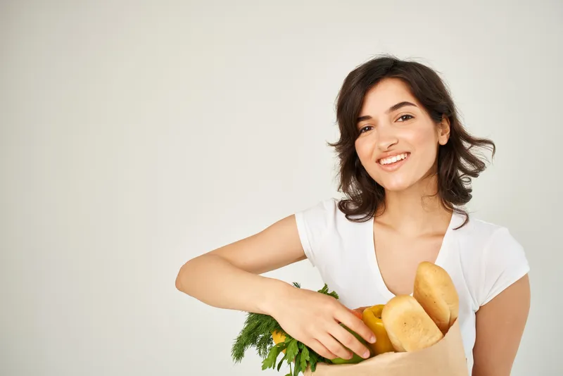 Весёлая брюнетка с продуктами и овощами на светлом фоне
